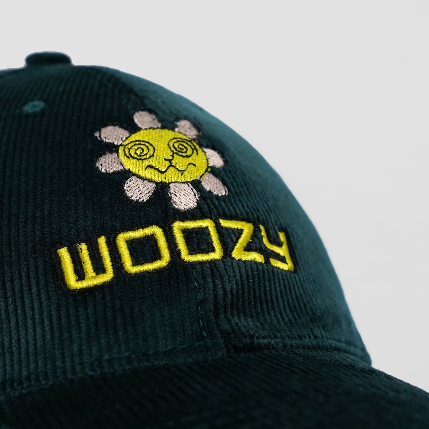 Dark green cap with embroidered sun design and 'Woozy' text on a light gray background