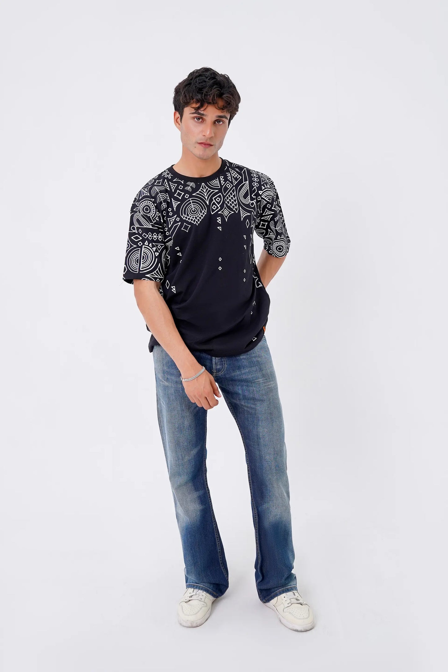 Person wearing a black patterned shirt and blue jeans on a white background