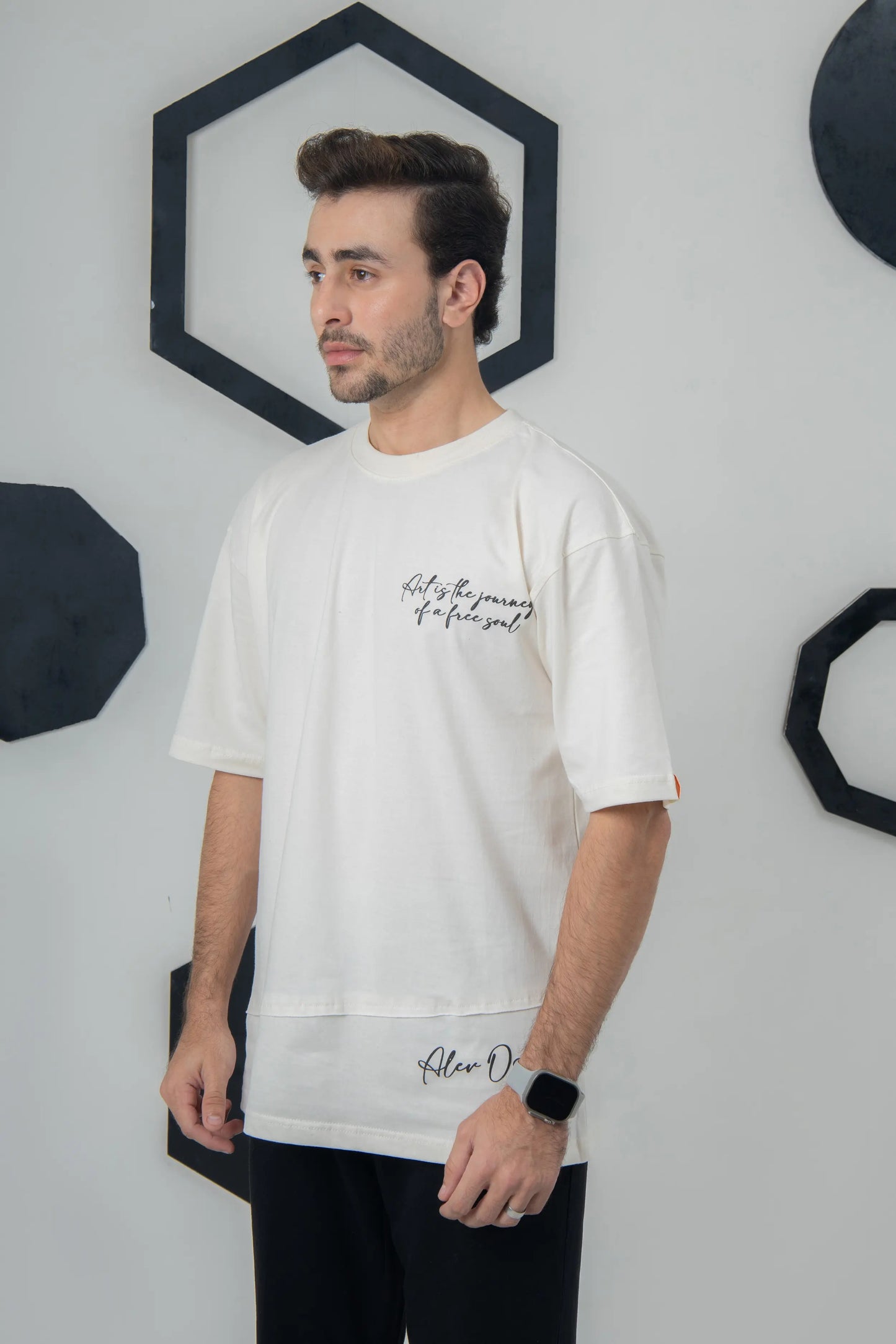 Man wearing a white t-shirt with text, standing against a geometric wall design.