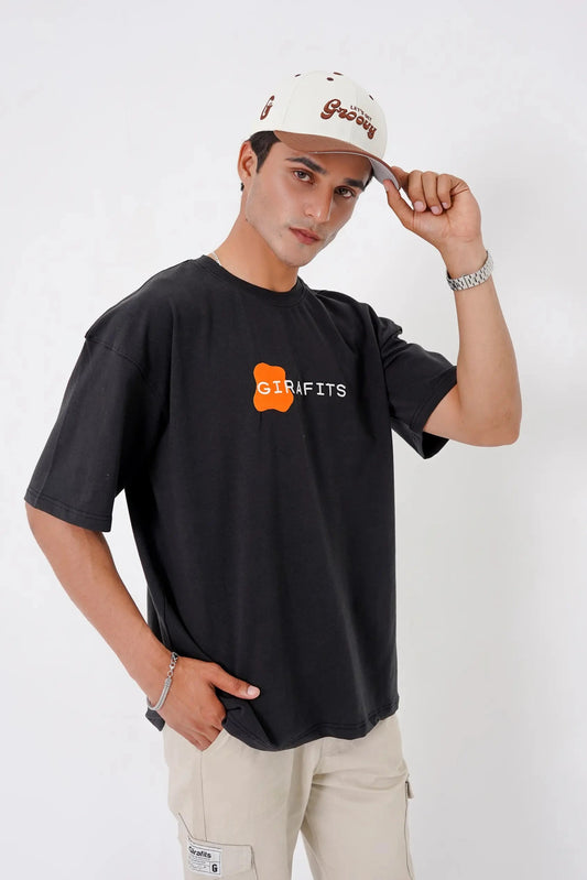 Person wearing a black t-shirt with a logo and text, beige pants, and a white cap on a white background
