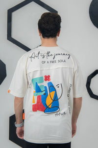 Person wearing a white t-shirt with colorful abstract design and text on the back, standing against a white wall with geometric black decorations.