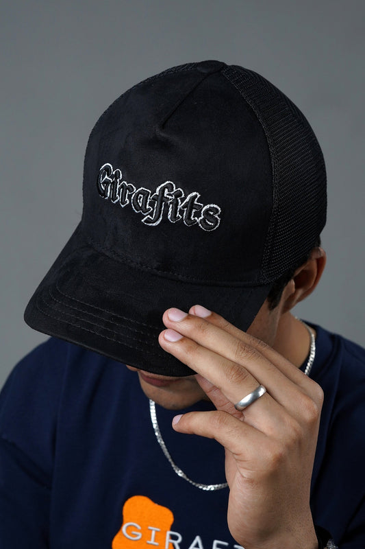 Person wearing a black cap with 'Graffitis' logo, covering face with hand on gray background